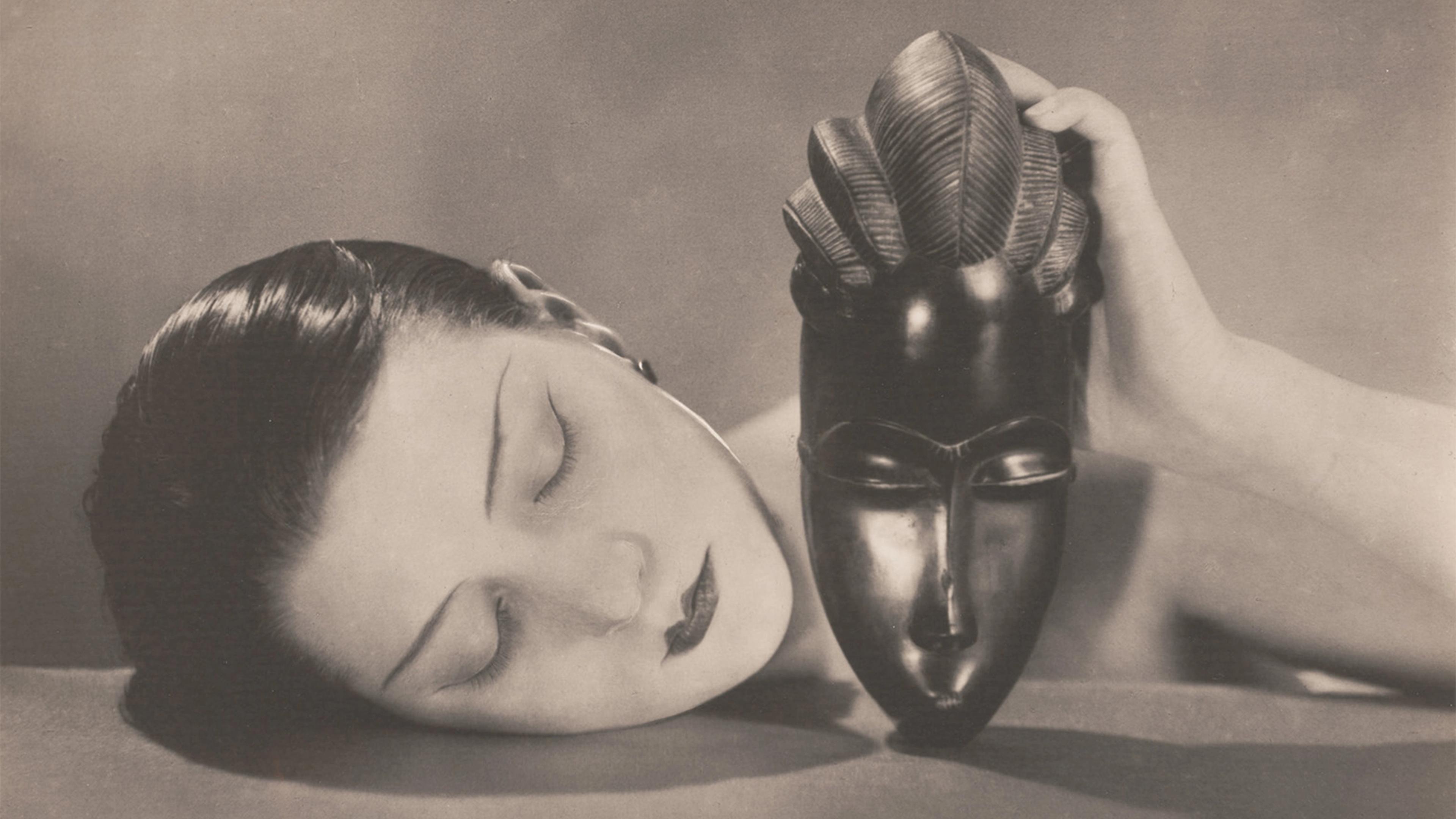 A woman with closed eyes rests her head on a surface, holding an ornate African mask. The sepia-toned image conveys a serene and introspective mood.