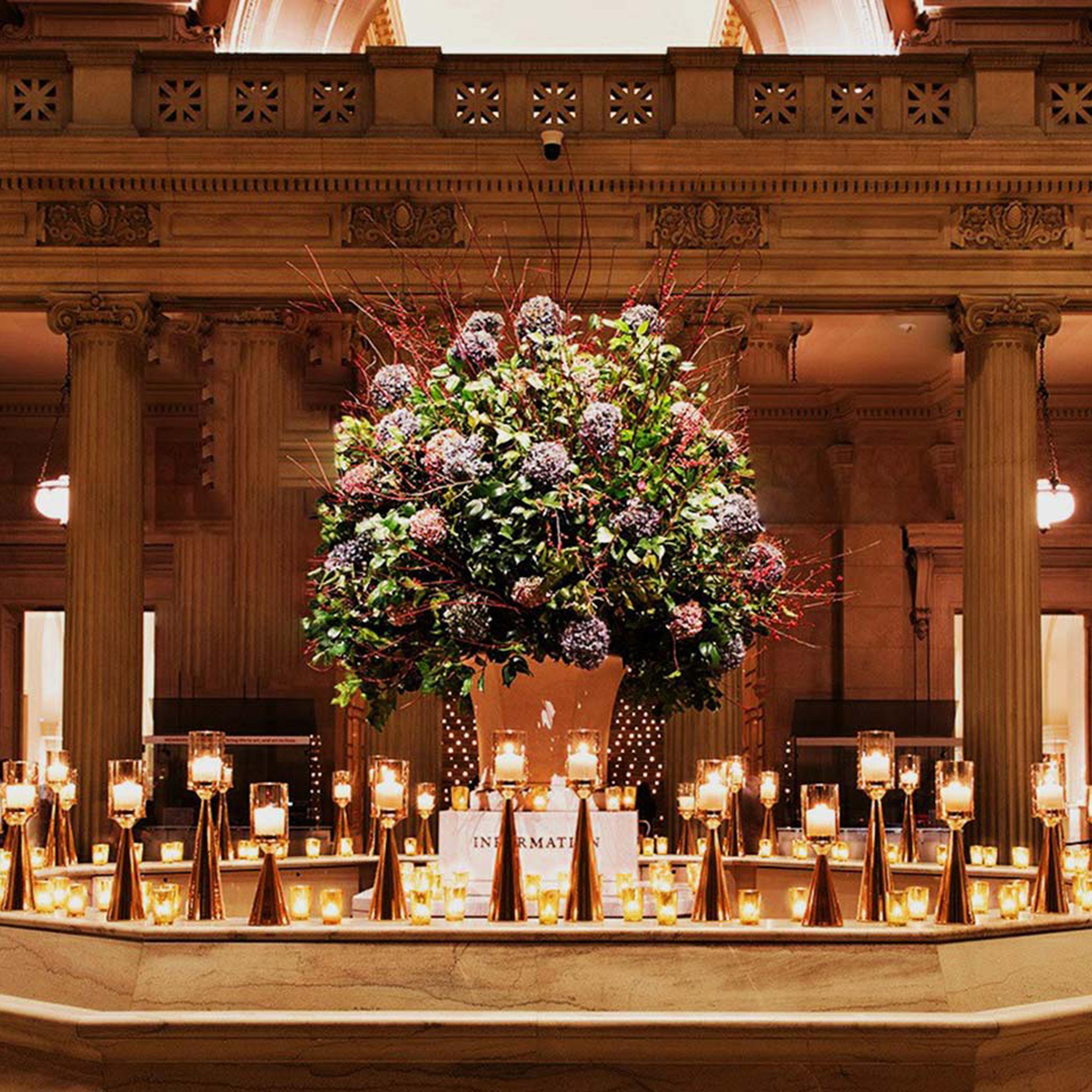 A candle-lit hexagonal marble information desk stands in the middle of a golden lit foyer