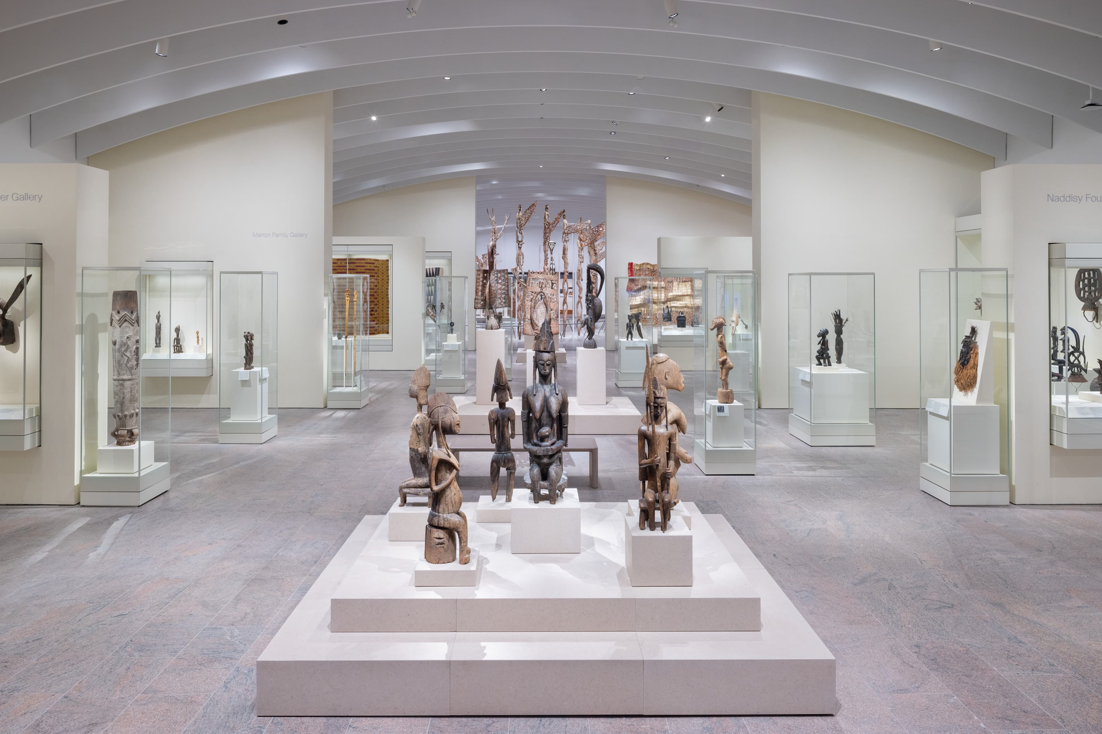 View of a gallery filled with wooden sculptures and artworks from Africa displayed inside glass cases.
