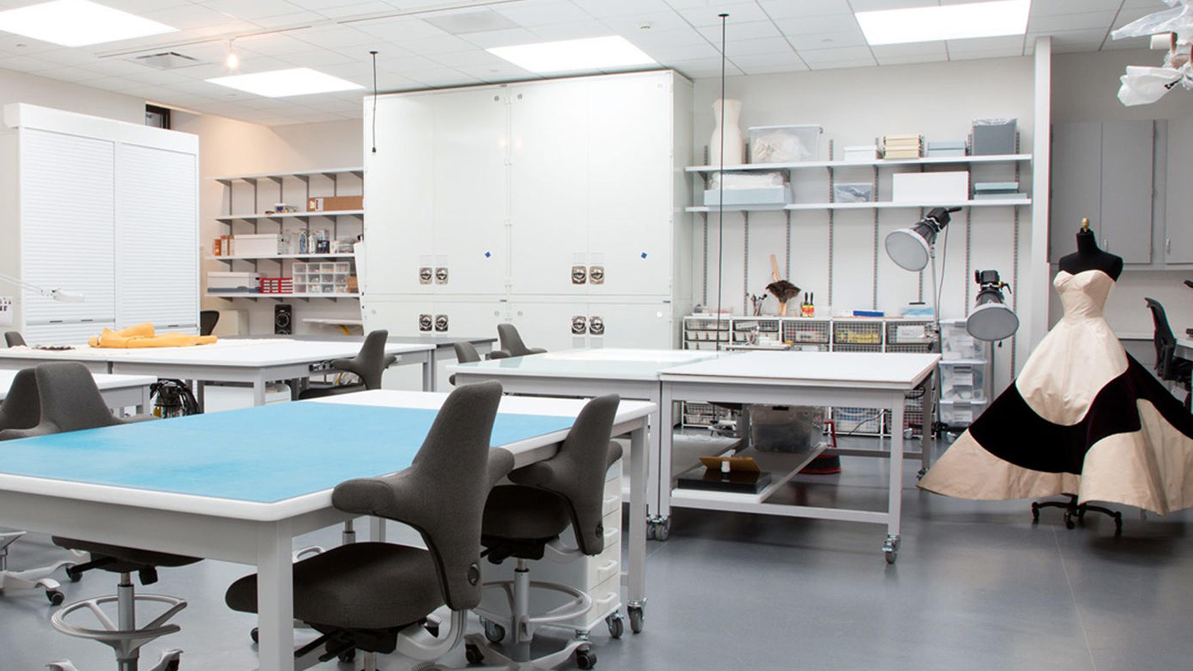 View of the Costume Institute Conservation lab, showing various examination tables, shelves of instruments, and a Charles James couture ballgown in the corner