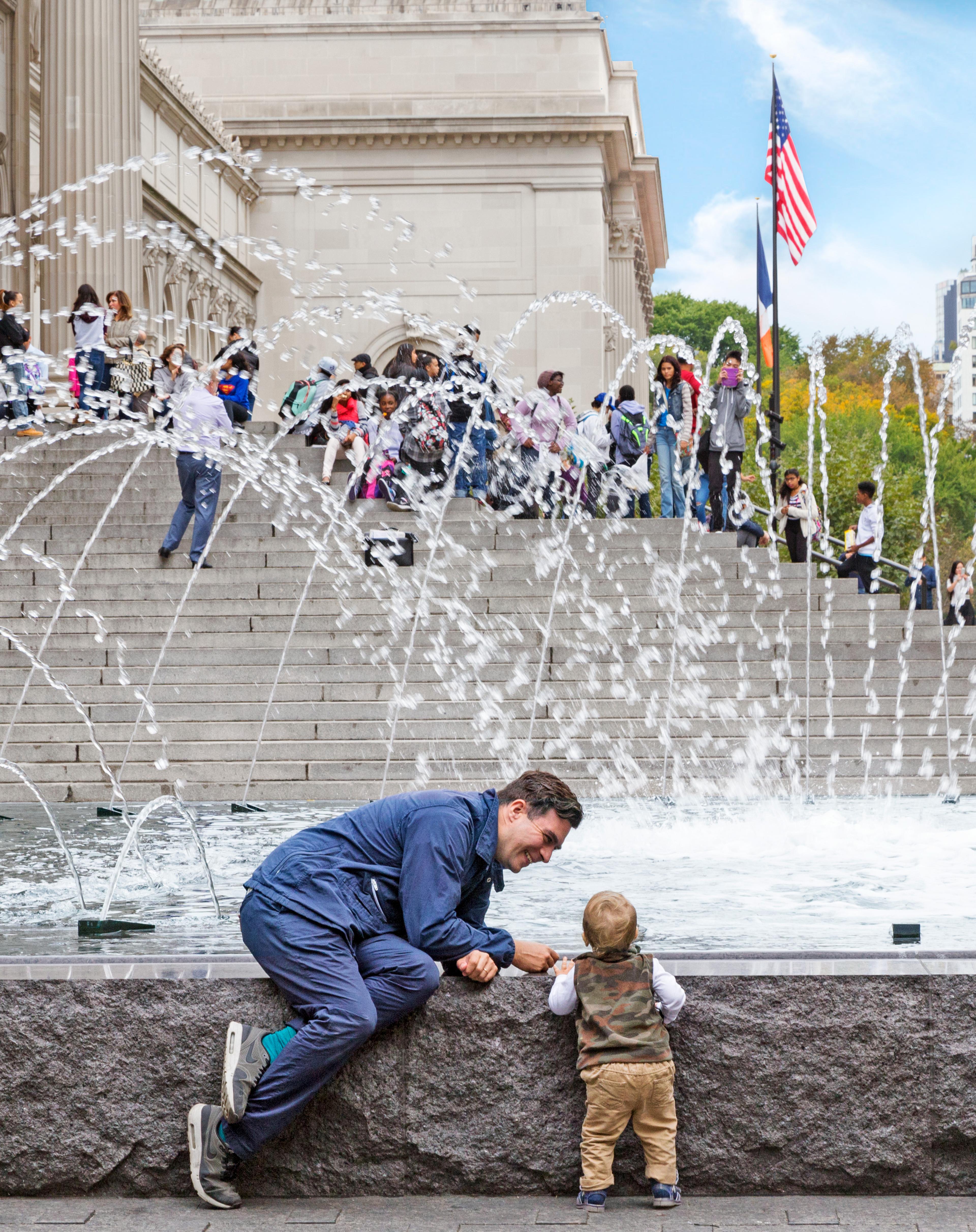 A father and a toddler hang out by the fountains on The Met Fifth Plaza.