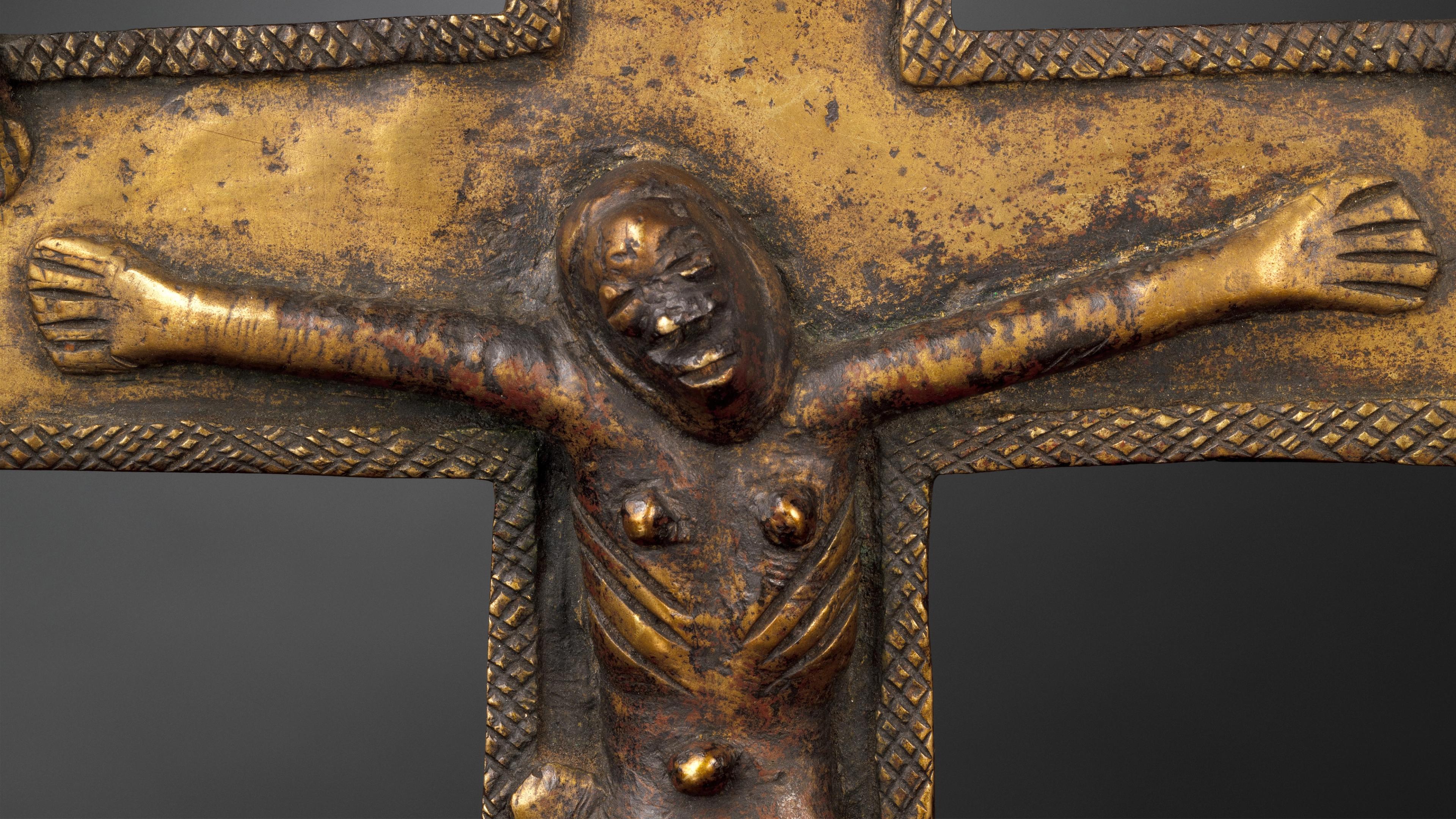 A Christ figure cast in relief, arms extended, on a brass cast crucifix.