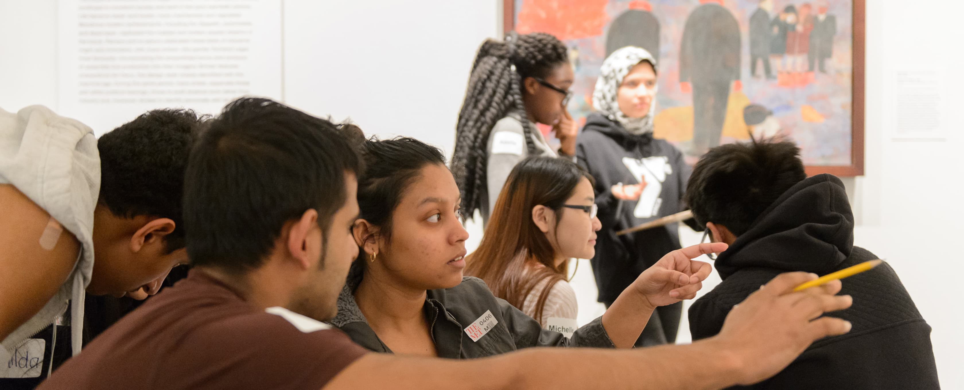 A group of young people observing and analyzing off-camera artwork in an art gallery.