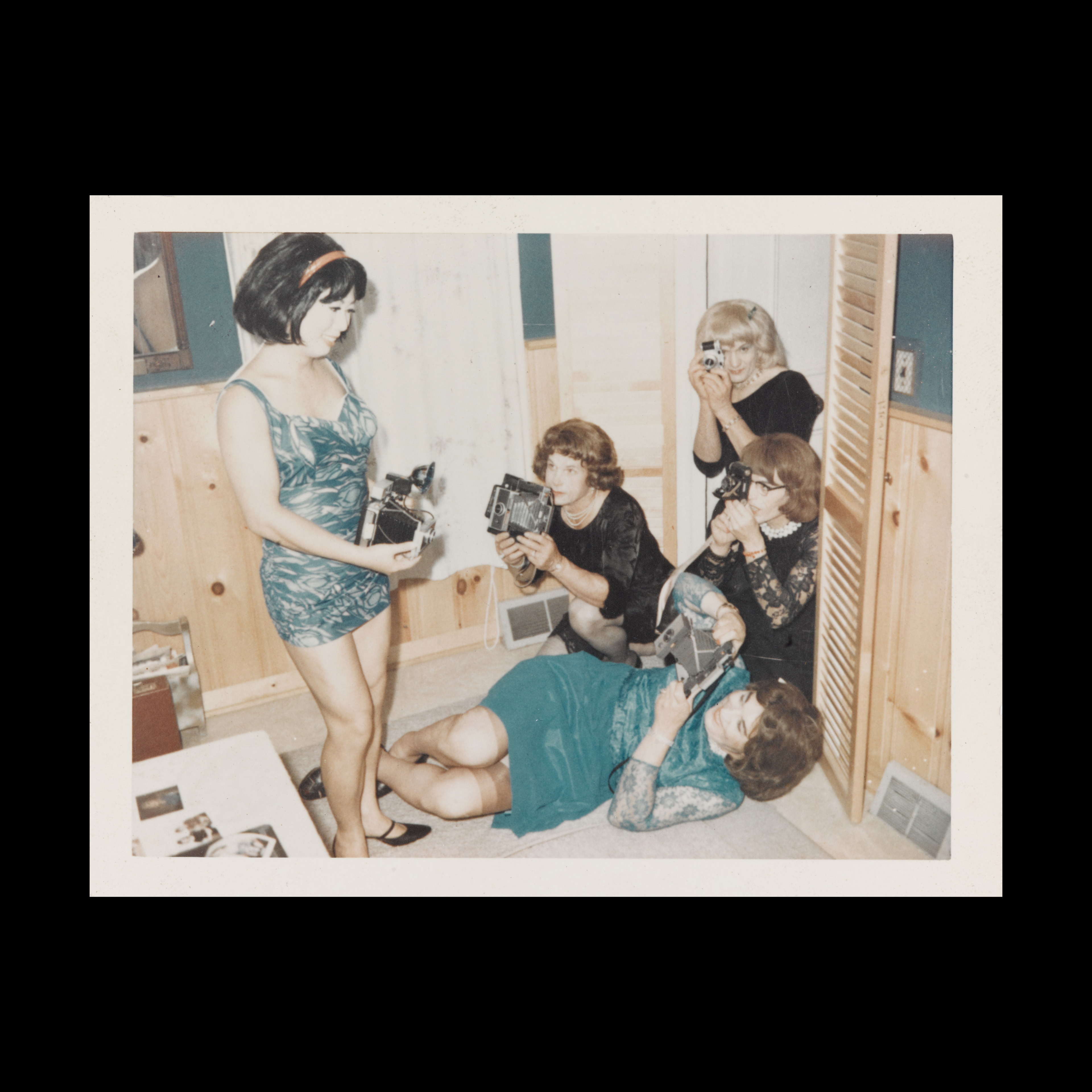 A group of women all wearing dresses, some black some green, and they all squat and stand as they take photos of one another.